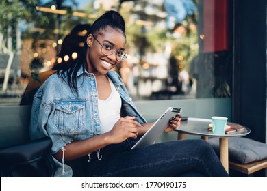 Portrait Of Cheerful Dark Skinned Woman Holding Digital Tablet Searching Information On Free Time, Young African American Female In Trendy Eyewear Satisfied With 4G Internet Connection Using Touchpad