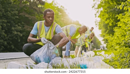 Portrait of cheerful and dedicated African American man as part of team of enthusiastic volunteers cleaning up area near road saving nature from pollution. Caring worker looking at camera with smile. - Powered by Shutterstock