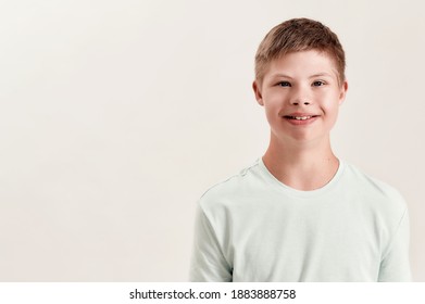 Portrait of cheerful disabled boy with Down syndrome smiling at camera while posing isolated over white background. Children with disabilities and special needs concept. Horizontal shot