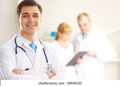 Portrait Of Cheerful Doctor Looking At Camera And Smiling With Working Clinicians Behind