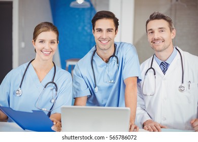 Portrait of cheerful doctors with laptop and clipboard while standing in hospital