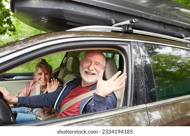 Portrait of cheerful elderly man and woman waving while traveling in car during road trip - Powered by Shutterstock