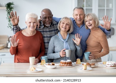 Portrait Of Cheerful Elderly Men And Women Spending Time Together, Multiracial Group Of Senior Friends Having Party At Home, Drinking Tea, Eating Cake, Waving At Camera And Smiling