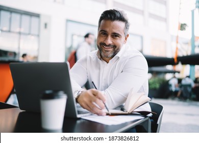 Portrait Of Cheerful Entrepreneur Dressed In Formal White Shirt Smiling At Camera During Time For Business Planning, Middle Aged Male Employer Working Remotely In Sidewalk Cafe Enjoying Lifestyle