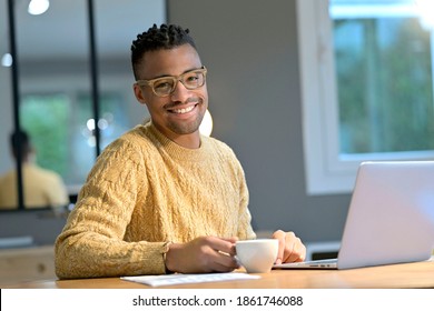 Portrait von fröhlichem ethnischen Typen, der von zu Hause aus arbeitet und eine Kaffeepause macht
