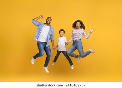 Portrait Of Cheerful Excited African American Family Of Three Holding Hands While Jumping In Air Over Yellow Background In Studio, Happy Black Parents And Preteen Son Having Fun Together, Copy Space - Powered by Shutterstock