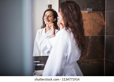 Portrait of cheerful female brushing teeth while looking at mirror - Powered by Shutterstock