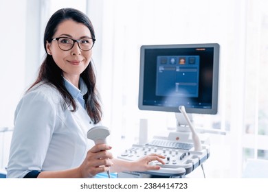 Portrait of cheerful female doctor with ultrasound sensor looking at the camera. Transducer. General practitioner radiologist ready to take mammography with medical equipment - Powered by Shutterstock