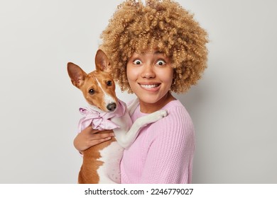 Portrait of cheerful female pet owner bites lips and looks surprisingly at camera poses with pedigree dog have good time together make common photo isolated over grey background. Love for pets - Shutterstock ID 2246779027