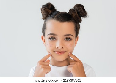 Portrait Of Cheerful Girl With Lip Gloss And Sparkling Glitter Stars Pointing At Face Isolated On Grey