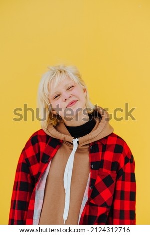 Portrait of a cheerful girl in a shirt and casual clothes on a background of yellow wall, looking at the camera and winking. Vertical