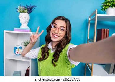 Portrait of cheerful girl toothy smile make selfie demonstrate v-sign isolated on blue color background
