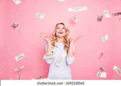 Portrait of cheerful glad girl enjoying shower from 100, hundred dollars, flying money, gesturing with hands isolated on pink background