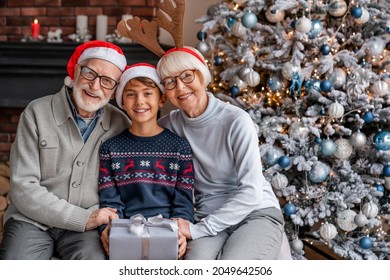 Portrait of cheerful grandparents with their grandson celebrating New Year near Christmas tree at home. Happy New Year and Merry Christmas - Powered by Shutterstock