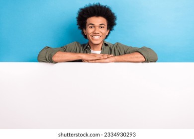 Portrait of cheerful guy with perming coiffure wear khaki shirt lean on white billboard empty space isolated on blue color background - Shutterstock ID 2334930293