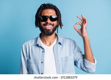 Portrait of cheerful handsome dark skin guy beaming smile fingers show okey symbol isolated on blue color background