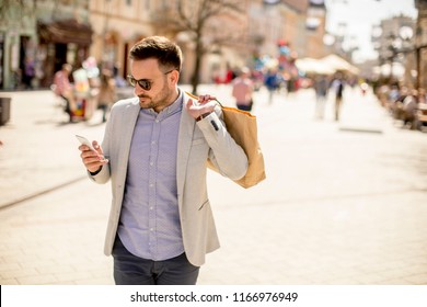 Portrait Of Cheerful Handsome Man Goes  Shopping In The City While Uses Mobile Phone