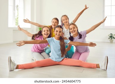 Portrait of cheerful happy active little girls sitting in the floor in choreography class, posing looking at camera and smiling. Group of cute kids having fun in dance. Children sport concept. - Powered by Shutterstock