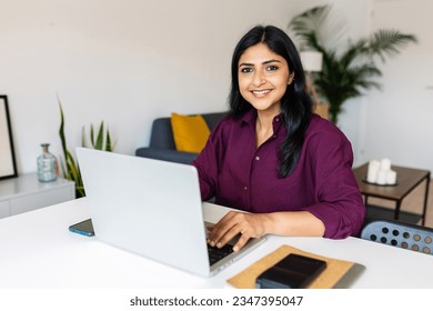 Portrait of cheerful indian business woman smile at camera using laptop at home. Entrepreneur and freelancer people concept.