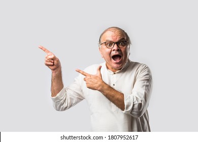 Portrait of cheerful Indian retired old man wears white kurta, pointing or presenting or in hands folded pose