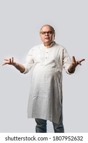 Portrait of cheerful Indian retired old man wears white kurta, pointing or presenting or in hands folded pose - Shutterstock ID 1807952632
