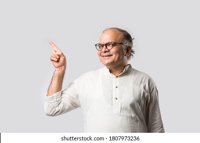 Portrait of cheerful Indian retired old man wears white kurta, pointing or presenting or in hands folded pose - Shutterstock ID 1807973236