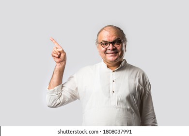 Portrait of cheerful Indian retired old man wears white kurta, pointing or presenting or in hands folded pose - Shutterstock ID 1808037991