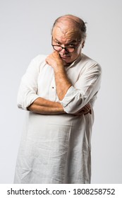 Portrait of cheerful Indian retired old man wears white kurta, pointing or presenting or in hands folded pose - Shutterstock ID 1808258752