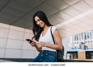 Portrait of cheerful Indian woman with beautiful face and smile using mobile phone for online shopping with discount sales. Successful asian blogger blog post into social networks, walking on street. 