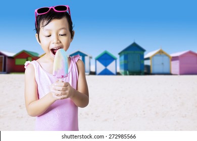 Portrait of cheerful kid standing on the shore while enjoy ice cream and wearing swimsuit - Powered by Shutterstock