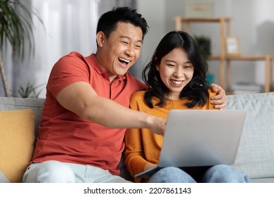 Portrait Of Cheerful Korean Spouses Using Laptop Together At Home, Happy Asian Middle Aged Man And Young Woman Sitting On Couch, Looking At Computer Screen And Smiling, Shopping Online, Copy Space