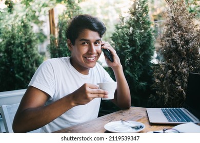 Portrait of cheerful Latin user calling to best friend for discussing meeting time, happy millennial hipster guy smiling at camera while making positive international conversation via mobile app