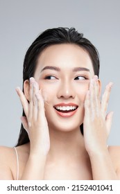 Portrait of cheerful laughing Asian woman applying foam for washing on her face with attractive appearance. Skincare spa relax concept. Isolated on grey background