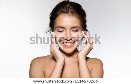 Portrait of cheerful laughing woman applying foam for washing on her face. Lovely brunette with attractive appearance. Skincare spa relax concept. Isolated on grey background