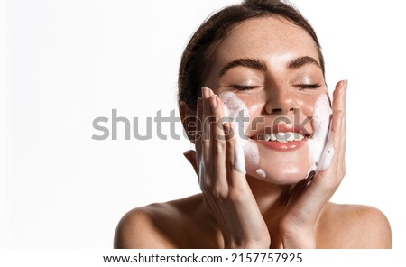 Portrait of cheerful laughing woman applying cleansing foam for washing face. Lovely brunette with attractive appearance. Skincare spa relax concept. Isolated on white background