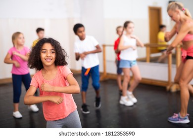 Portrait Of Cheerful Little African American Girl Training Movements During Group Class In Dance School