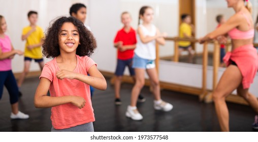 Portrait Of Cheerful Little African American Girl Training Movements During Group Class In Dance School