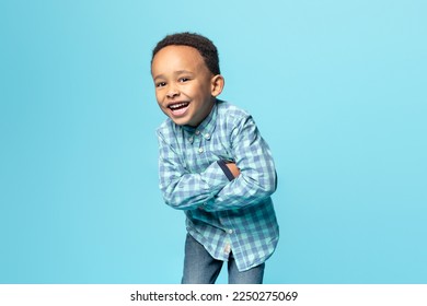 Portrait of cheerful little african american boy posing with folded arms over blue background, joyful male kid in stylish shirt smiling and looking at camera, copy space - Powered by Shutterstock