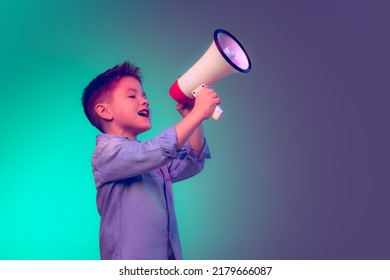 Portrait Of Cheerful Little Boy, Child Shouting In Megaphone, Posing Isolated Over Green Purple Background In Neon Light. Concept Of Childhood, Family, Emotions, Lifestyle, Fashion, Ad