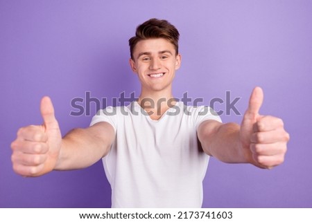 Portrait of cheerful man in basic clothing smiling showing thumbs up at camera isolated over shine background