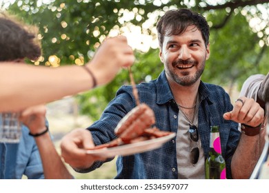 Portrait of cheerful man sharing food during outdoor gathering. Natural candid moment of friendship and happiness with genuine smile during sunset picnic - Powered by Shutterstock