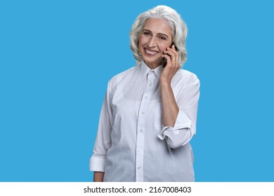 Portrait Of Cheerful Mature Business Lady Talking On Mobile Phone. Smiling Senior Woman Talking On Cell Phone On Blue Background.