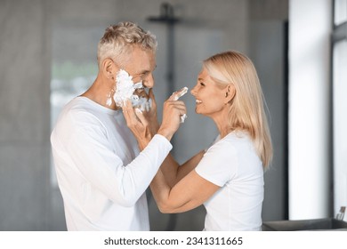 Portrait Of Cheerful Mature Couple Having Fun In Bathroom, Happy Senior Spouses Fooling Together While Getting Ready In The Morning, Playing With Shaving Foam And Laughing At Home, Side View - Powered by Shutterstock