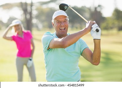 Portrait of cheerful mature golfer holding golf club while standing on field