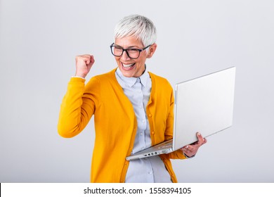 Portrait Of A Cheerful Mature Woman With A Laptop Computer And Celebrating Success Isolated Over Gray Background. Senior Lady Watching Celebrating Online Bid Bet Win Or Great Result Victory Concept