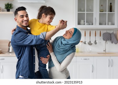 Portrait Of Cheerful Middle Eastern Family Of Three Having Fun In Kitchen Together, Happy Islamic Parents Bonding With Their Little Daughter And Laughing, Enjoying Spending Time At Home, Free Space