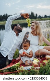 Portrait Of Cheerful Mixed Race Family Eating Some Food Having Picnic Outdoors.