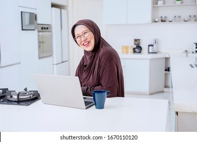 Portrait Of Cheerful Old Woman Laughing While Sitting With Laptop In Kitchen