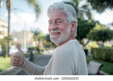 Portrait of cheerful optimist senior man looking at camera with thums up. Elderly bearded caucasian male in outdoor in urban park enjoying retirement - Powered by Shutterstock