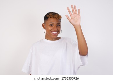 Portrait Of Cheerful, Outgoing Friendly-looking Young Woman Wearing Casual Clothes Raise One Hand And Wave, Saying Hi Or Hello And Smiling With Carefree Expression As Make Goodbye Or Welcome Gesture.